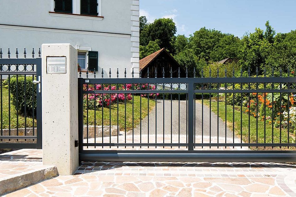 Schiebetor und Gartentür aus Aluminium in Kunstschmiede-Optik vor großer Gartenanlage