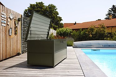 Gartenbox in anthrazit steht auf einer Terrasse neben einem großen Pool 