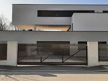 Schiebetor aus Aluminium von Super-Zaun mit Latten und Schrägkappen vor einer Einfahrt zu einem modernen Einfamilienhaus