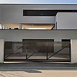 Schiebetor im Stil eines Lattenzauns mit Schrägkappen vor einer Einfahrt eines modernen Einfamilienhauses