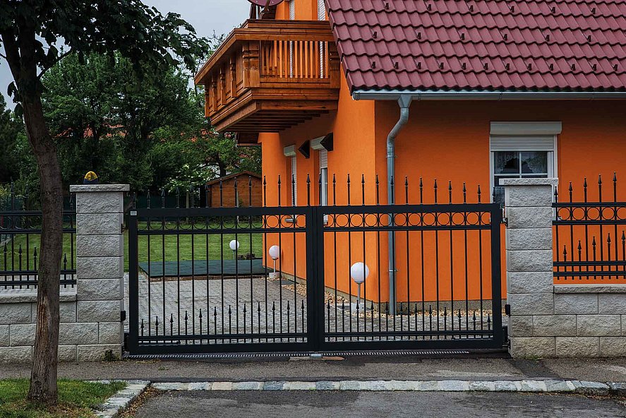 Doppelflügeltor aus schwarzen Stäben aus Aluminium zum Stabzaun um ein orangenes Haus