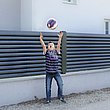 Kind wirft Ball vor Gartenzaun mit Lamellen in anthrazit auf weißem Mauersockel