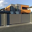 Gartentür und Schiebetor aus grauen Lamellen nvor modernem Architektenhaus in orange und grau