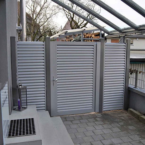 Bild eines Hauseingangs, dessen Durchgang durch ein blickdichtes Gartentor aus Aluminium in grau abgegrenzt wird