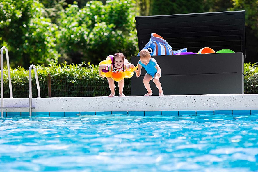 Auflagenbox in anthrazit hinter Kindern die in den Pool springen