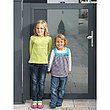 zwei Mädchen lehnen an einer Lochblechtür in der Einfahrt zum Haus