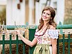 [Translate to Fransösich:] junge Frau in Dirndl steht vor grünem Palisadenzaun mit silbernen Zaunkappen in Kugelform