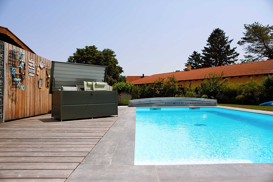 Gartenbox aus Stahl in anthrazit mit eingebautem Schloss steht in einem Garten neben einem Pool