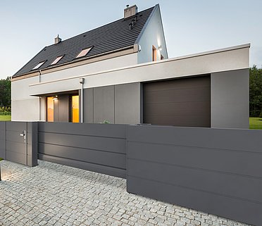 Blickdichte Gartentür und dazu passendes Schiebetor aus Aluminium in anthrazit, dahinter ein kleines, modernes Einfamilienhaus