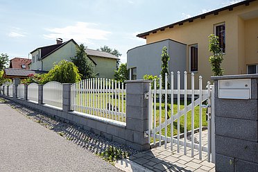 Geschwungene Gartentüre mit dazu passendem Gartenzaun aus Rundstäben in weiß auf einer Mauer montiert