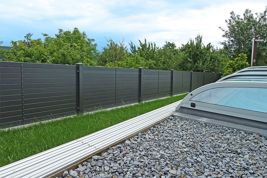 Blick vom überdachten Pool im Garten auf modernen Gartenzaun mit Querlatten aus Aluminium und Sichtschutz