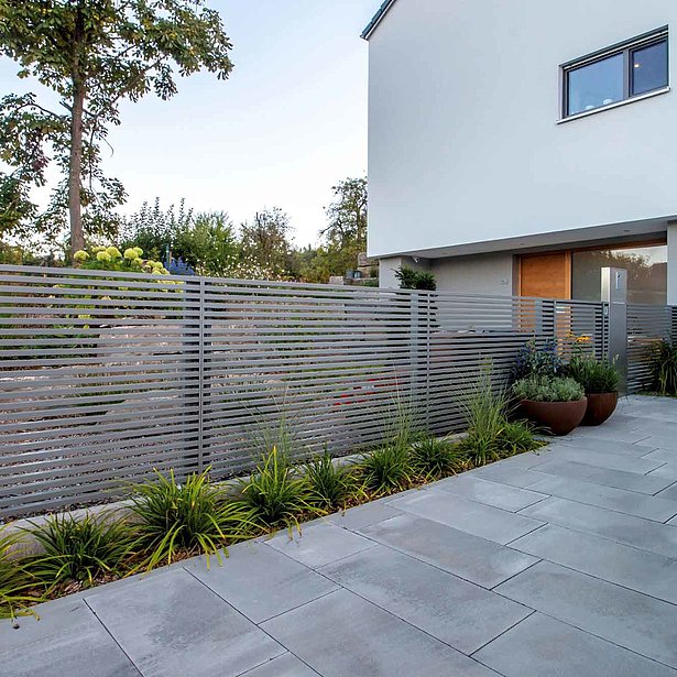 Moderner Gartenzaun mit Querlatten aus Aluminium vor einem modernen Eigenheim in graualuminium