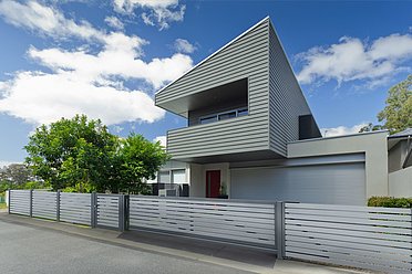 Modernes Schiebetor mit Querlatten aus Aluminium in grau und dazu passendem Gartenzaun vor einem außergewöhnlichen Einfamilienhaus