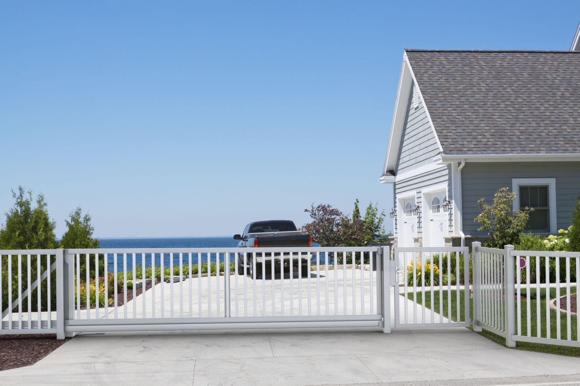 weißer Stabzaun mit Schiebetor und Gartentür vor Haus am Meer