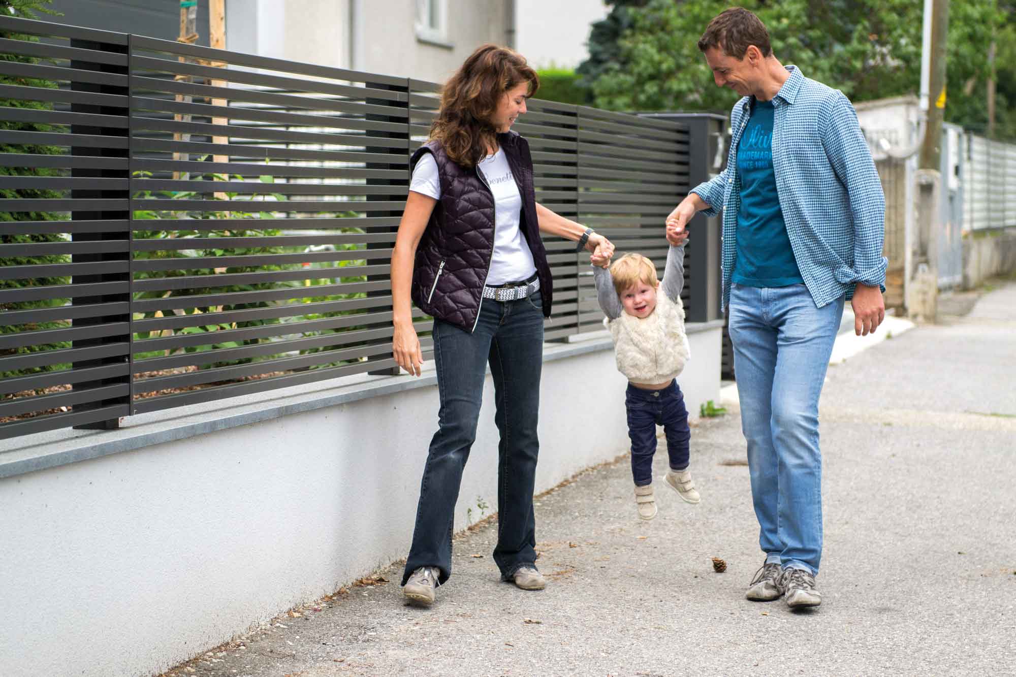 Familie mit Kind vor modernem Gartenzaun mit horizontalen Latten in anthrazit